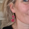 Boucles d'oreilles portées en résine de couleur rouge légèrement pailletée, longueur de 45 mm, avec des variations de couleur.