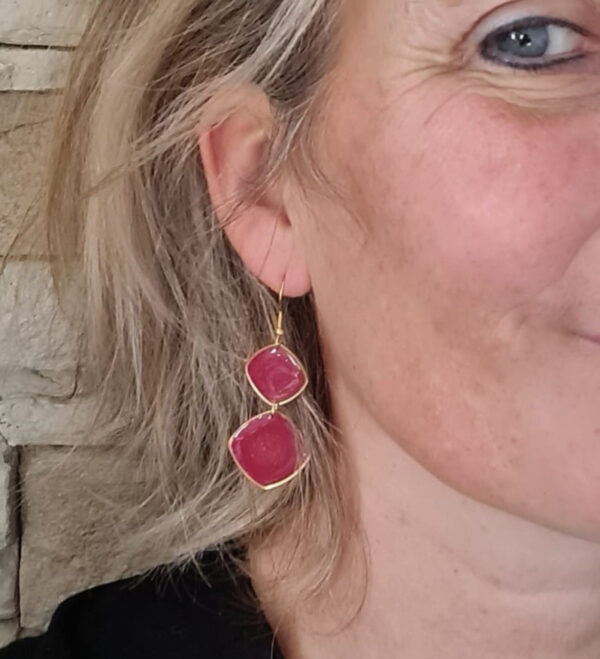 Boucles d'oreilles portées en résine de couleur rouge légèrement pailletée, longueur de 45 mm, avec des variations de couleur.