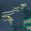 Détail des Boucles d'oreilles pendantes en perles de rocaille tissées à la main, dans des tons verts, dorés et sombres. Élégantes et géométriques, elles ajoutent une touche unique et sophistiquée à toute tenue.