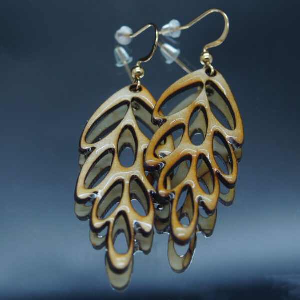 Paire de boucles d’oreilles en bois finement découpé, inspirée des formes naturelles d’une feuille ou d’une algue stylisée. Leur design ajouré apporte une impression de légèreté, sublimée par une finition brillante en résine. Montées sur des crochets dorés en acier inoxydable avec embouts en silicone, ces boucles sont à la fois élégantes et légères. Un bijou délicat qui capture l’harmonie et la beauté de la nature.