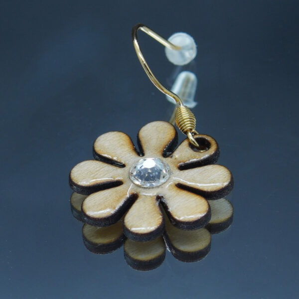 Boucle d’oreille en forme de marguerites d'un diamètre de 20 mm, réalisées en bois finement découpé avec des pétales délicatement définis. La fleur est ornée d’un crystal scintillant en son centre, ajoutant une touche lumineuse et élégante.