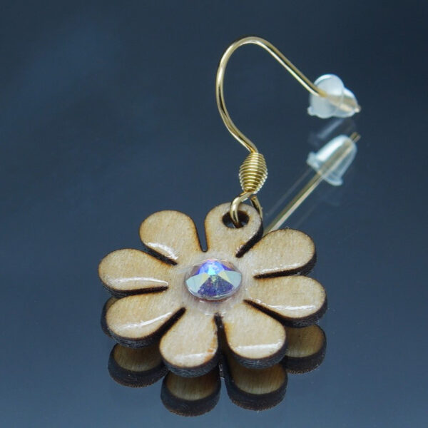 Boucle d’oreille en forme de marguerites d'un diamètre de 20 mm, réalisées en bois finement découpé avec des pétales délicatement définis. La fleur est ornée d’un crystal rainbow scintillant en son centre, ajoutant une touche lumineuse et élégante.