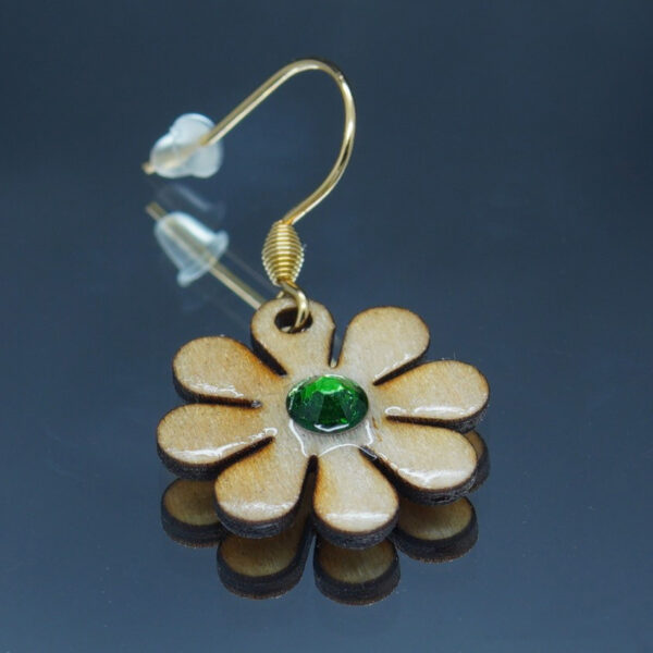 Boucle d’oreille en forme de marguerites d'un diamètre de 20 mm, réalisées en bois finement découpé avec des pétales délicatement définis. La fleur est ornée d’un strass vert scintillant en son centre, ajoutant une touche lumineuse et élégante.