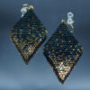 Paire de boucles d’oreilles en forme de losange, tissées à la main avec des perles Cube Miyuki aux nuances dorées et bleutées, créant un effet scintillant et profond. Les reflets subtils rappellent un ciel étoilé. Montées sur des crochets dorés en acier inoxydable avec embouts en silicone, ces boucles sont légères et confortables à porter.