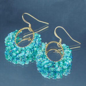 Paire de boucles d'oreilles élégantes de forme oblongue, confectionnées avec des perles en déclinaison de bleu, scintillantes et délicates. Les perles sont minutieusement assemblées sur des arcs métalliques dorés, créant un design harmonieux et sophistiqué. Le crochet d’attache doré ajoute une touche classique et raffinée, parfait pour sublimer une tenue de soirée ou apporter une touche chic au quotidien. Ces bijoux reflètent un artisanat soigné et une attention particulière aux détails.