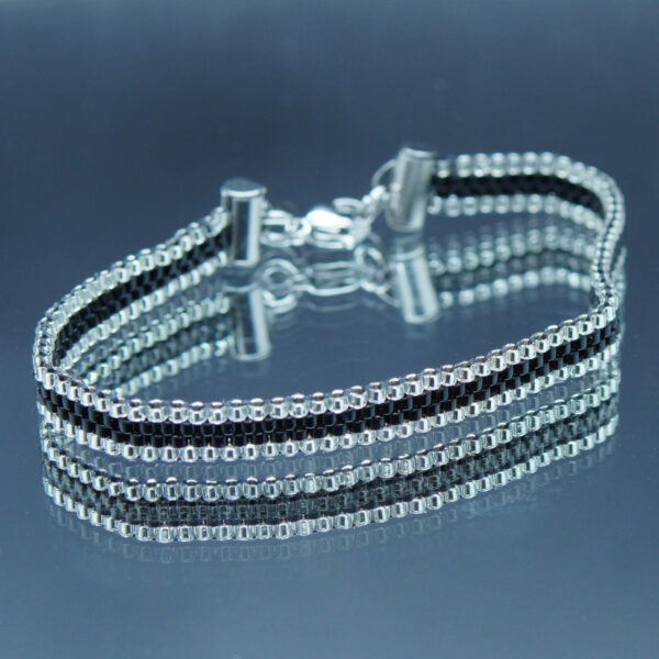 Bracelet tissé à la main sur 4 rangs avec perles Miyuki argentées et noires, et finitions en acier inoxydable doré. Un bijou élégant et raffiné, au design fin et lumineux.