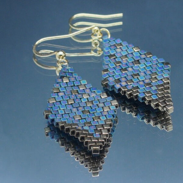 Paire de boucles d’oreilles en forme de losange, tissées à la main avec des perles Cube Miyuki aux nuances de bronze et de bleu de gris, créant un effet scintillant et profond. Les reflets subtils rappellent un ciel étoilé. Montées sur des crochets dorés en acier inoxydable avec embouts en silicone, ces boucles sont légères et confortables à porter.