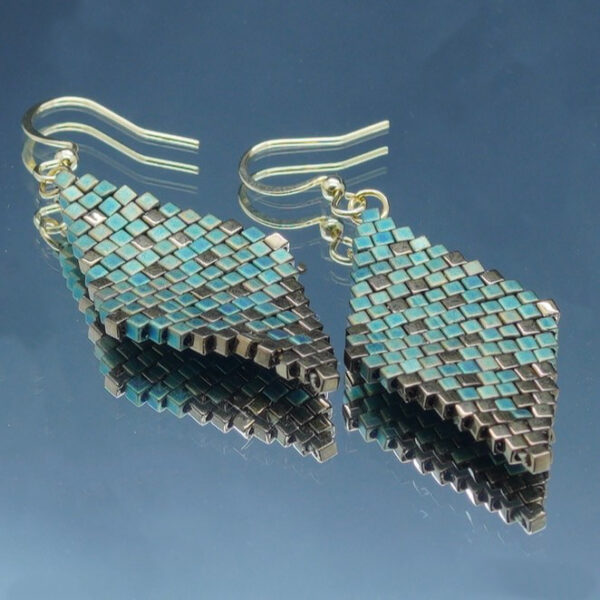 Paire de boucles d’oreilles en forme de losange, tissées à la main avec des perles Cube Miyuki aux nuances de bronze et de vert de gris, créant un effet scintillant et profond. Les reflets subtils rappellent un ciel étoilé. Montées sur des crochets dorés en acier inoxydable avec embouts en silicone, ces boucles sont légères et confortables à porter.