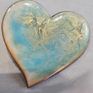 Broche artisanale en forme de cœur et en bois gravé, décorée de bleu avec des reflets d'or.
