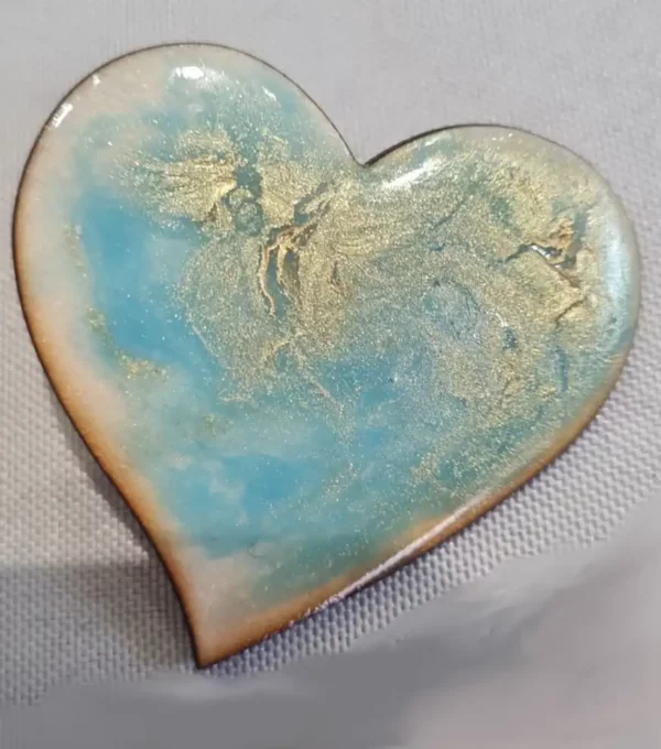 Broche artisanale en forme de cœur et en bois gravé, décorée de bleu avec des reflets d'or.