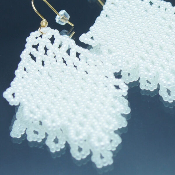 Boucles d'oreilles pendantes en dentelles de perles blanches, formant un motif délicatement tissé. Montées sur des crochets dorés, elles offrent un effet fluide et scintillant, parfait pour une touche d’élégance et de raffinement.