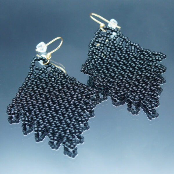 Boucles d'oreilles pendantes en dentelles de perles noires, formant un motif délicatement tissé. Montées sur des crochets dorés, elles offrent un effet fluide et scintillant, parfait pour une touche d’élégance et de raffinement.