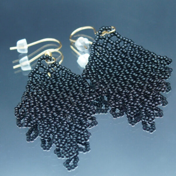 Boucles d'oreilles pendantes en dentelles de perles noires, formant un motif délicatement tissé. Montées sur des crochets dorés, elles offrent un effet fluide et scintillant, parfait pour une touche d’élégance et de raffinement.
