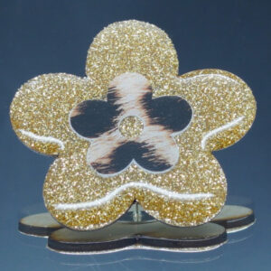Broche artisanale en forme de fleur et en bois gravé, décorée d’un motif doré pailleté entourant une fleur motif léopard.