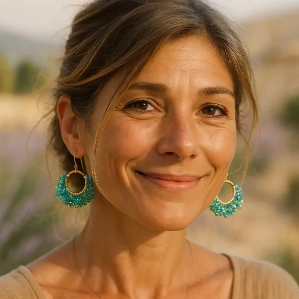 Modèle portant une paire de boucles d'oreilles élégantes, confectionnées avec des perles en déclinaison de bleu et de vert, scintillantes et délicates. Les perles sont minutieusement assemblées sur des arcs métalliques dorés, créant un design harmonieux et sophistiqué. Le crochet d’attache doré ajoute une touche classique et raffinée, parfait pour sublimer une tenue de soirée ou apporter une touche chic au quotidien. Ces bijoux reflètent un artisanat soigné et une attention particulière aux détails.